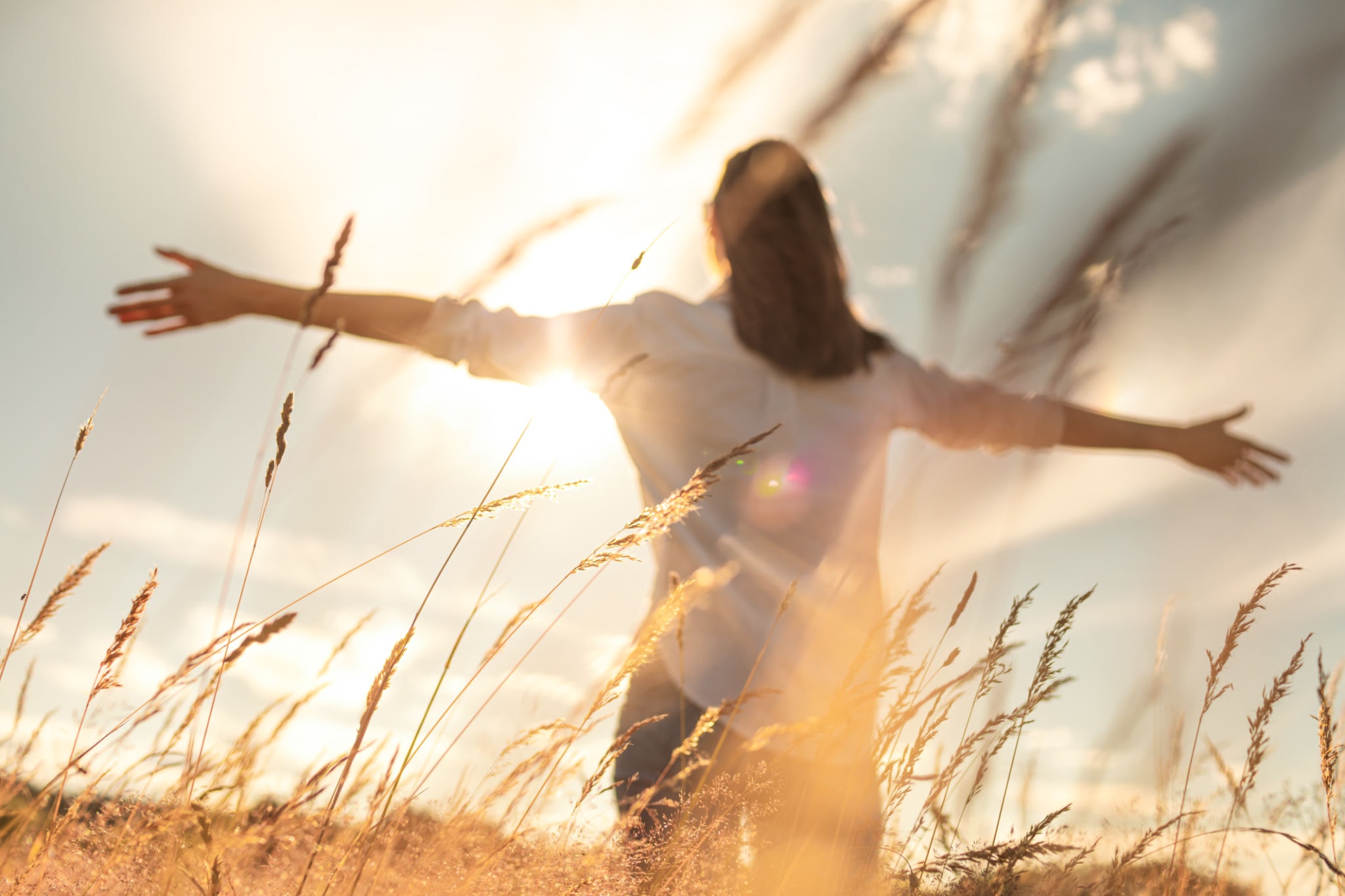 Woman in a field with arms outstretched at golden hour